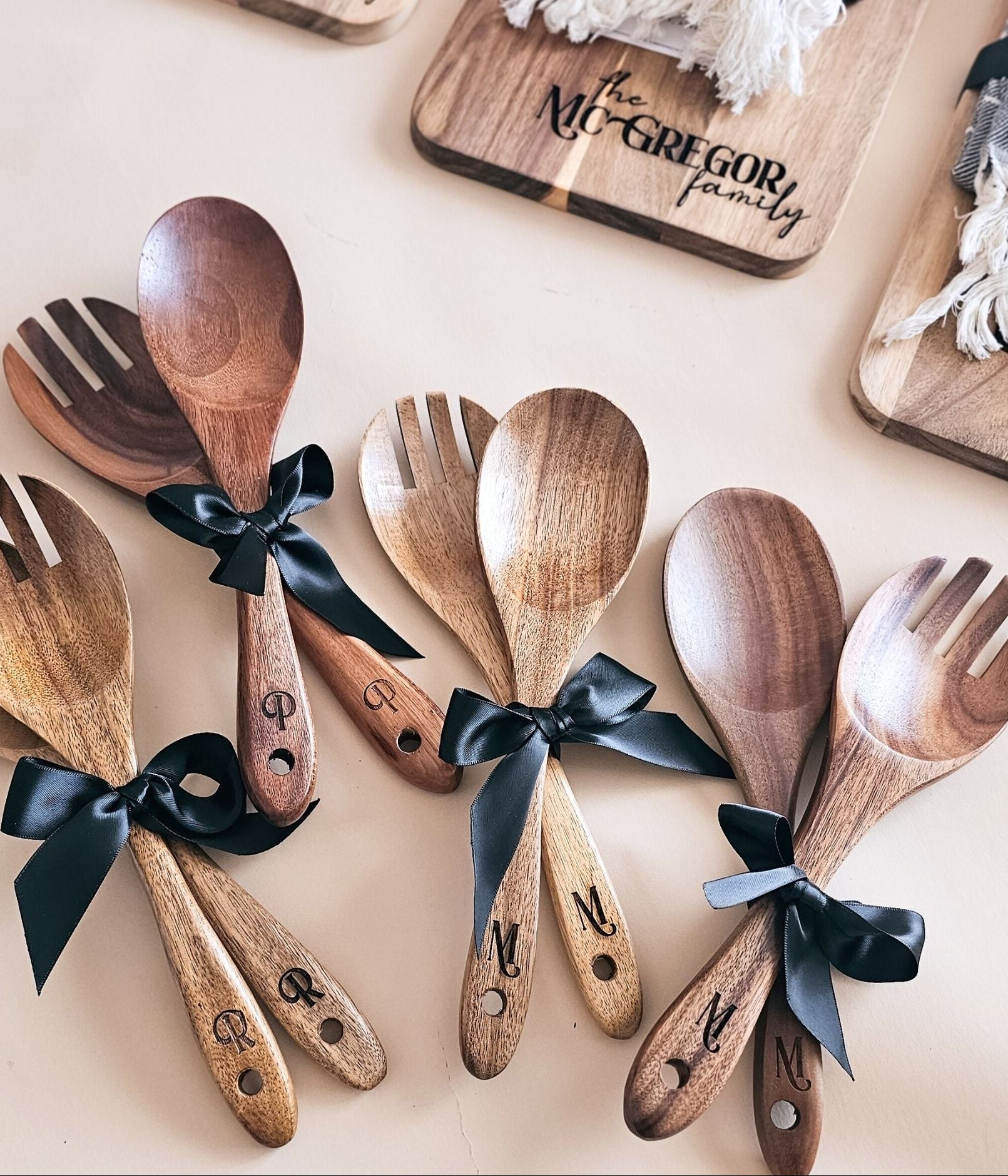 Wooden spoons and forks with personalized initials on handles, tied with black ribbons, on a light background.