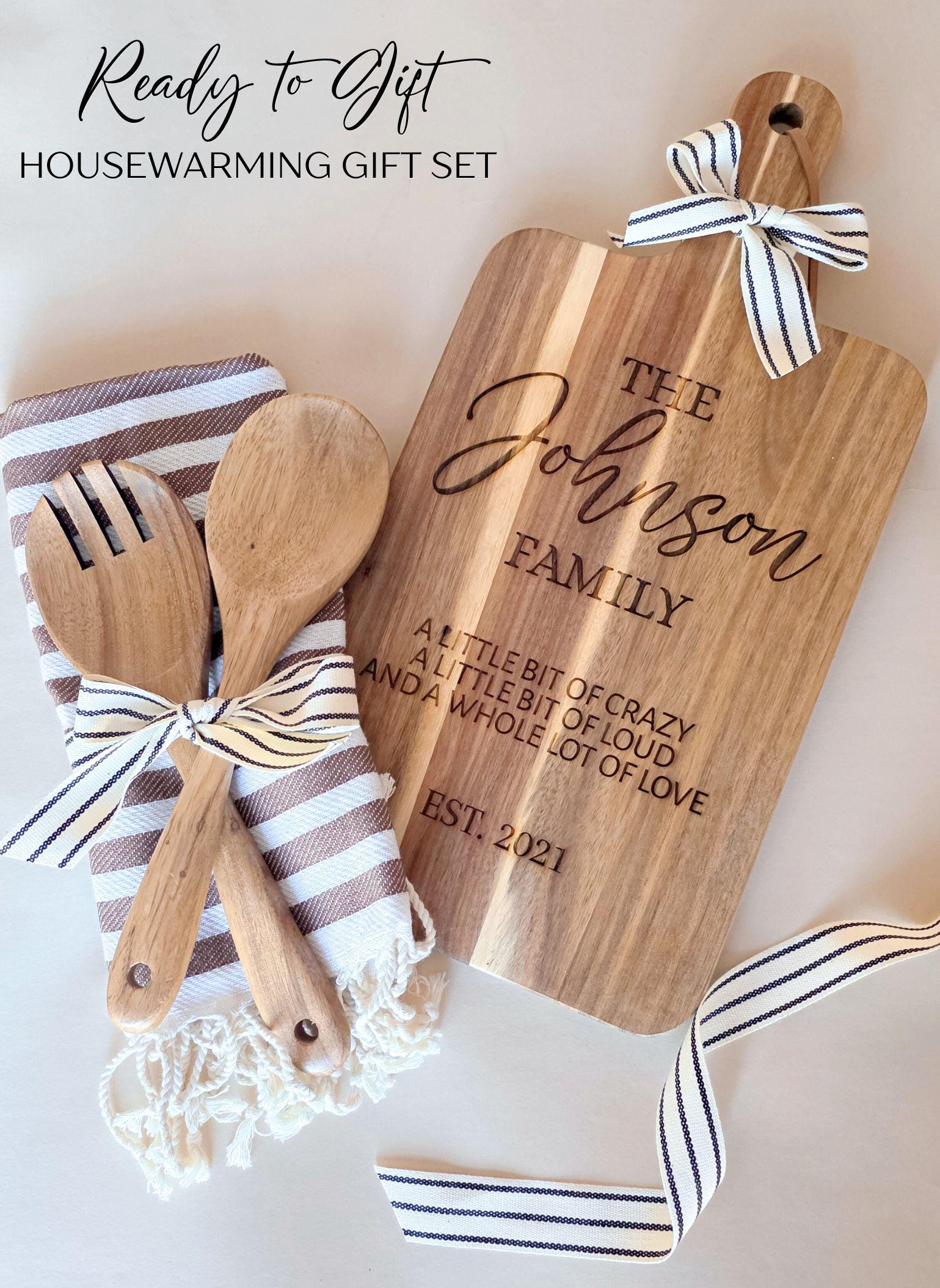Personalized housewarming gift set with engraved family name cutting board, striped towel and wooden utensils, ready to gift
