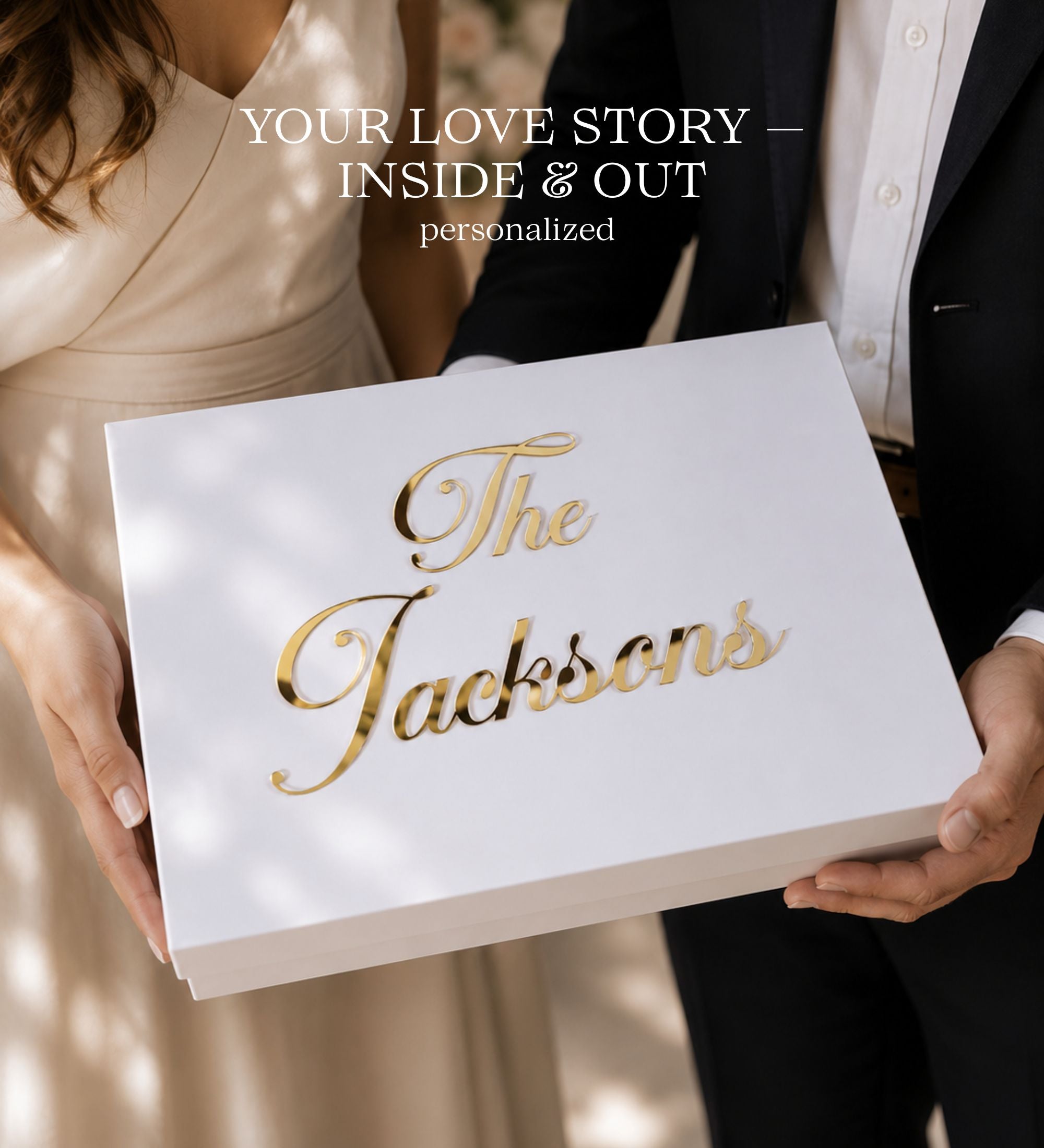 A white personalized keepsake box with metallic gold foil script reading 'The Jacksons' is held by a man in a black suit and a woman in a cream dress. Text overlay at the top reads 'YOUR LOVE STORY — INSIDE & OUT personalized'.