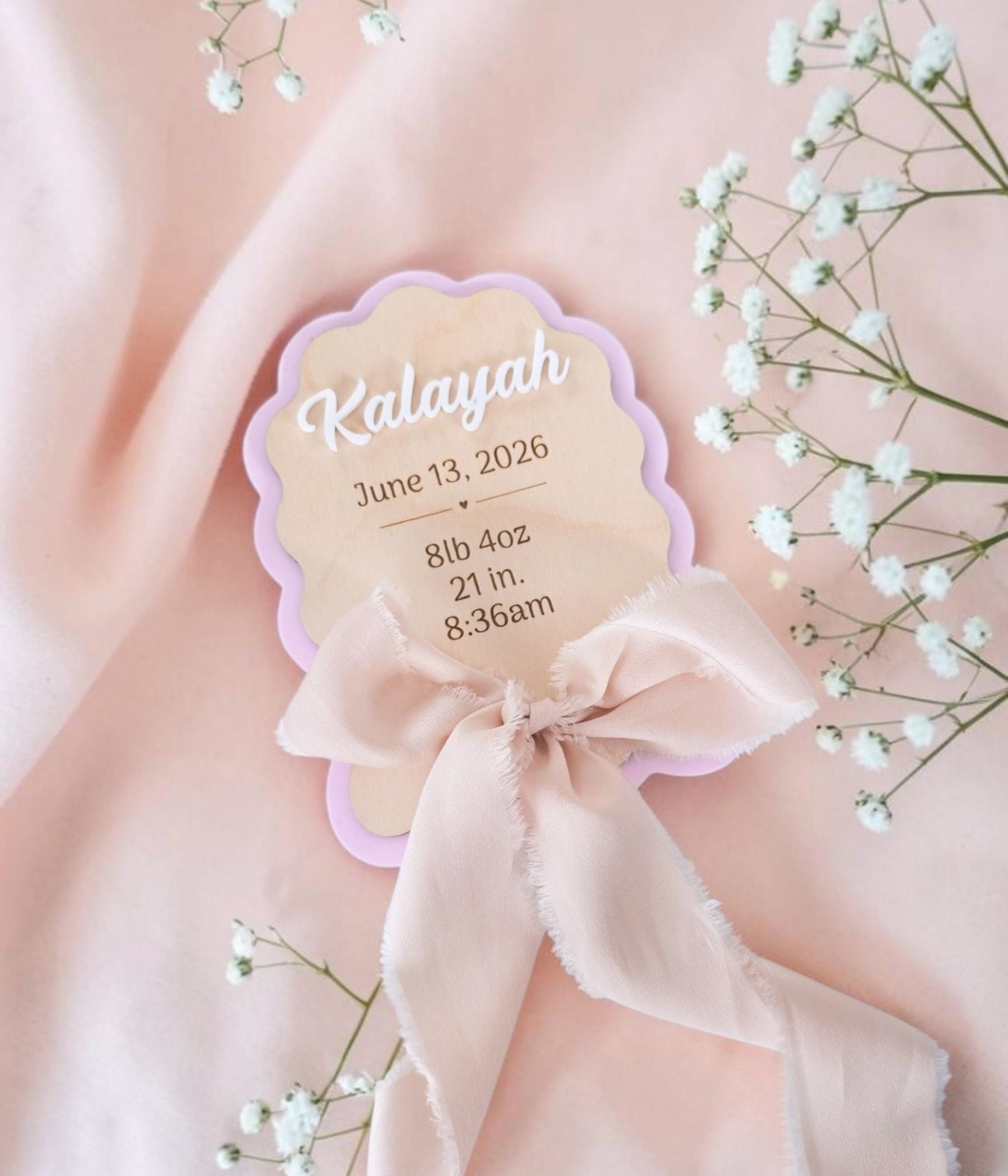 Scalloped wood and acrylic newborn keepsake sign with chiffon blush bow, shown as hospital photo prop on textured white surface