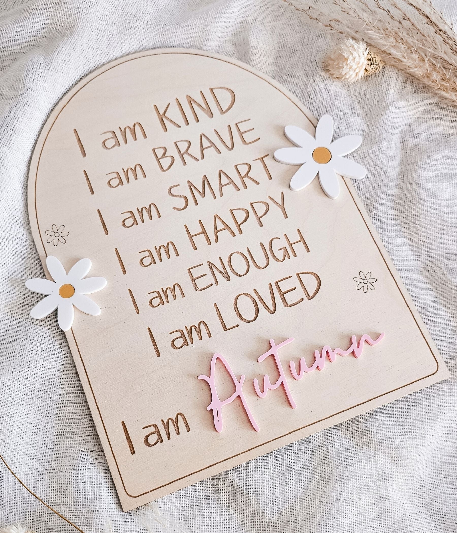 Close-up of engraved affirmations “I am kind, brave, smart” on wooden arch sign with daisy accents