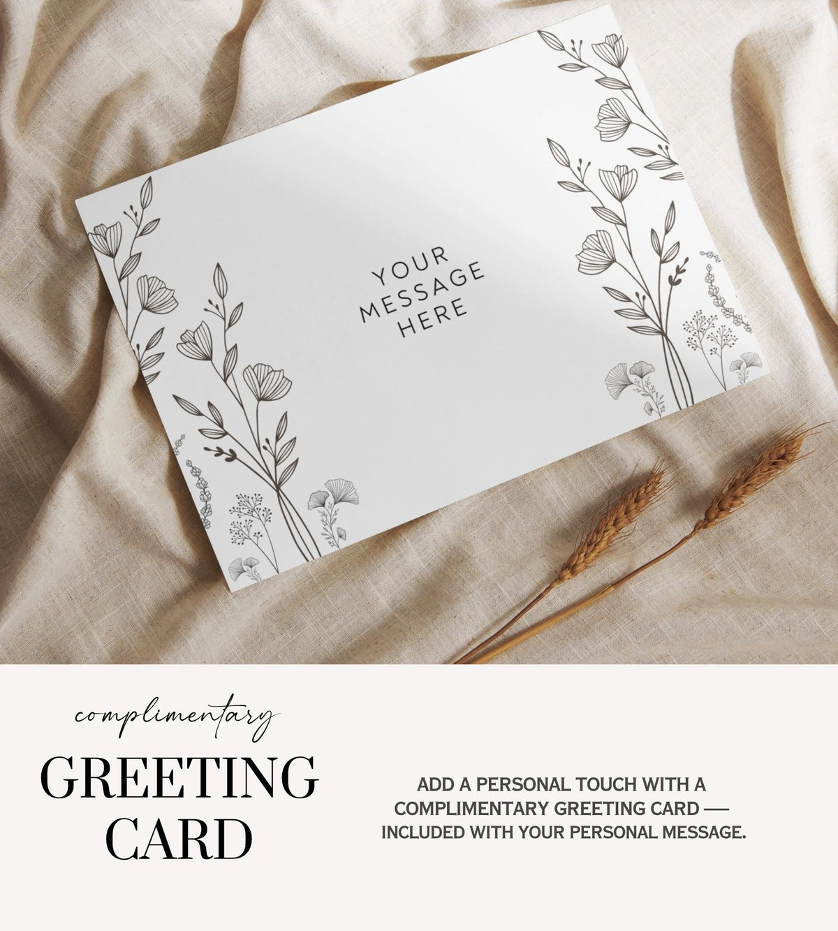 A white greeting card with delicate black floral line art and the text 'YOUR MESSAGE HERE' is shown on draped beige fabric, with wheat stems beside it. Text below reads 'complimentary GREETING CARD' and says to add a personal touch with a complimentary greeting card included with personal message.