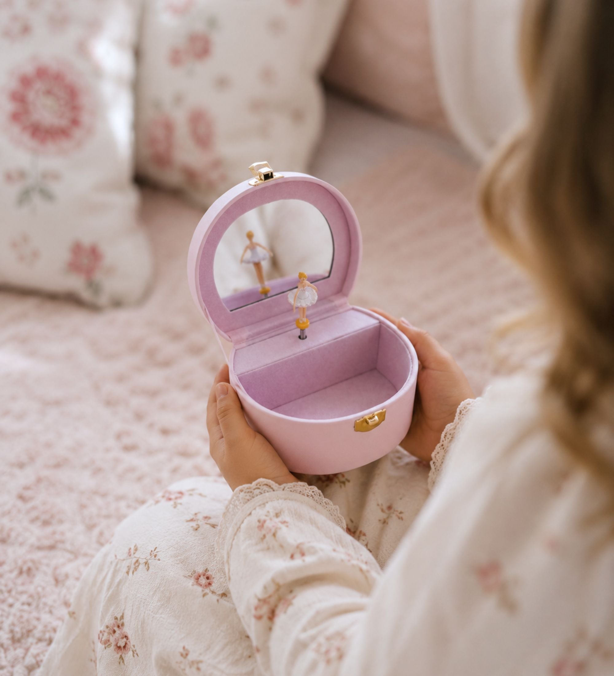 Young girl's hands opening a pink leatherette musical jewelry box, spinning ballerina visible inside lid mirror, jewelry and hair accessories inside