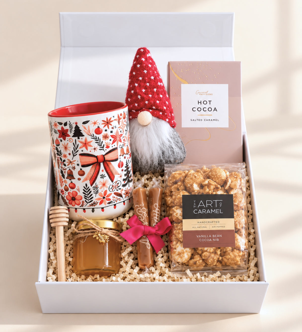 Top-down view of an open magnetic gift box filled with a festive mug, red-hat gnome, salted caramel hot cocoa, caramel popcorn, honey jar and artisan caramels
