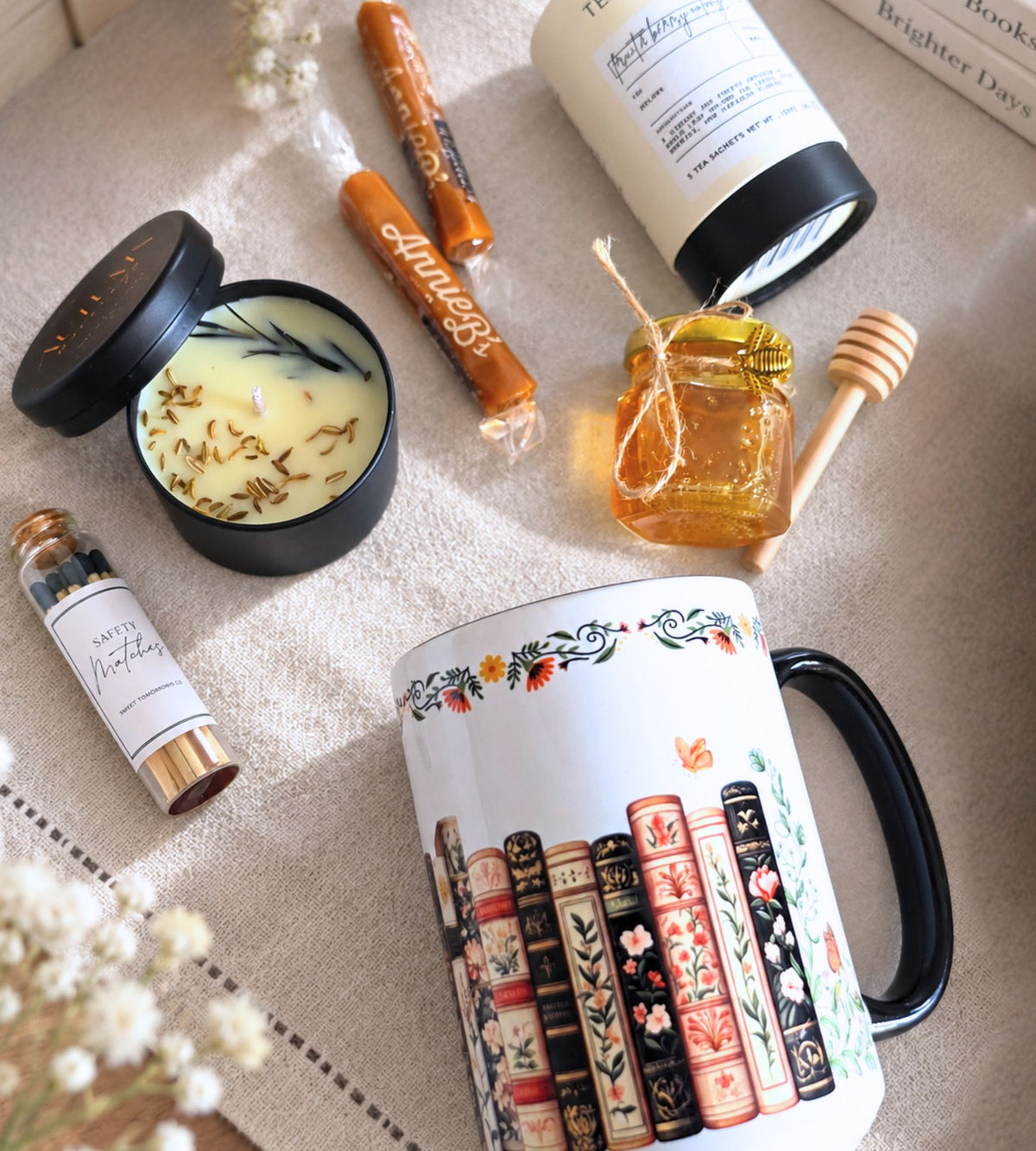 Flat lay of the candle, caramel sticks, honey jar with wooden dipper, and tea tin arranged beside the illustrated mug