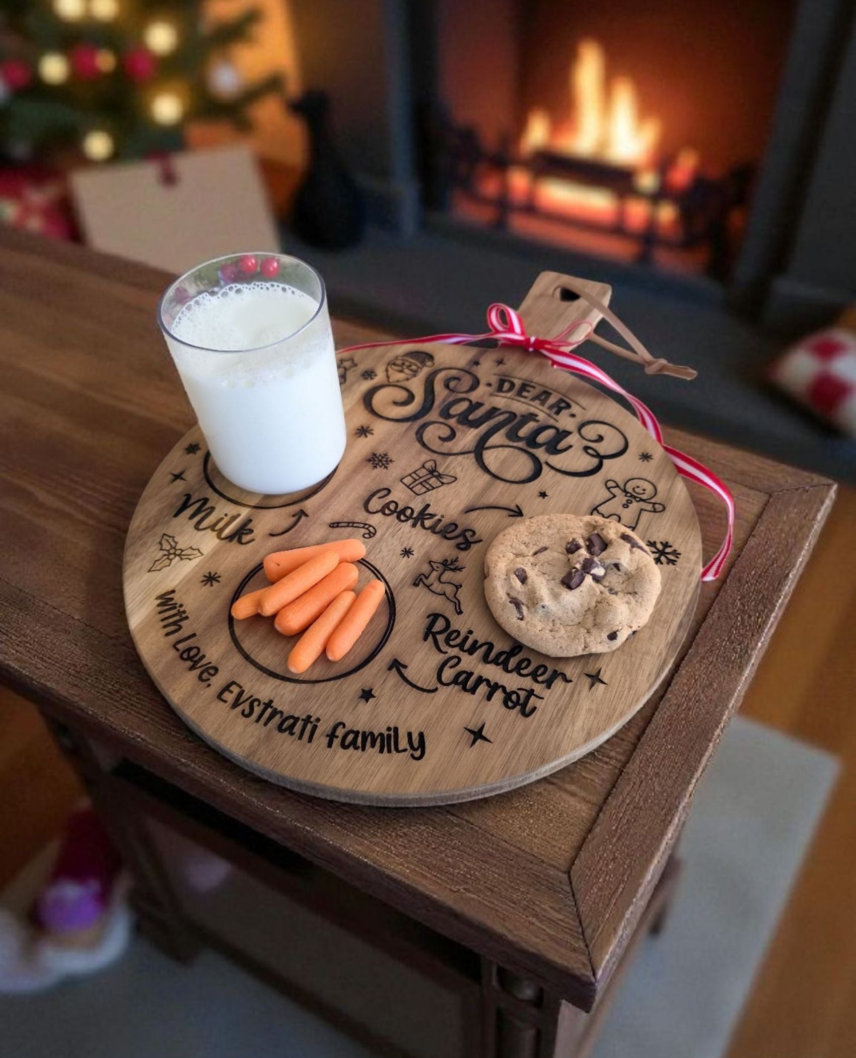 Personalized Santa treat board in acacia holding a glass of milk, a chocolate chip cookie, and carrots, with a red ribbon on the handle