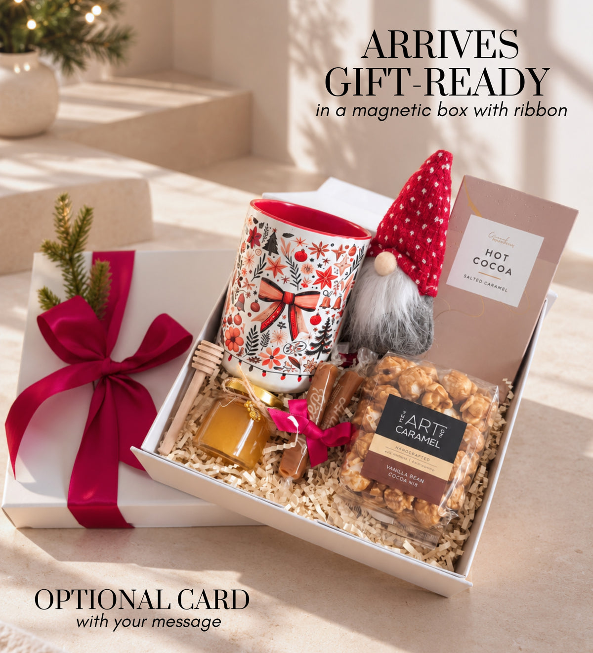 Gift-ready Christmas box with a berry-red ribbon on the lid, opened to show the mug, gnome, cocoa, honey, caramels and popcorn on paper shred