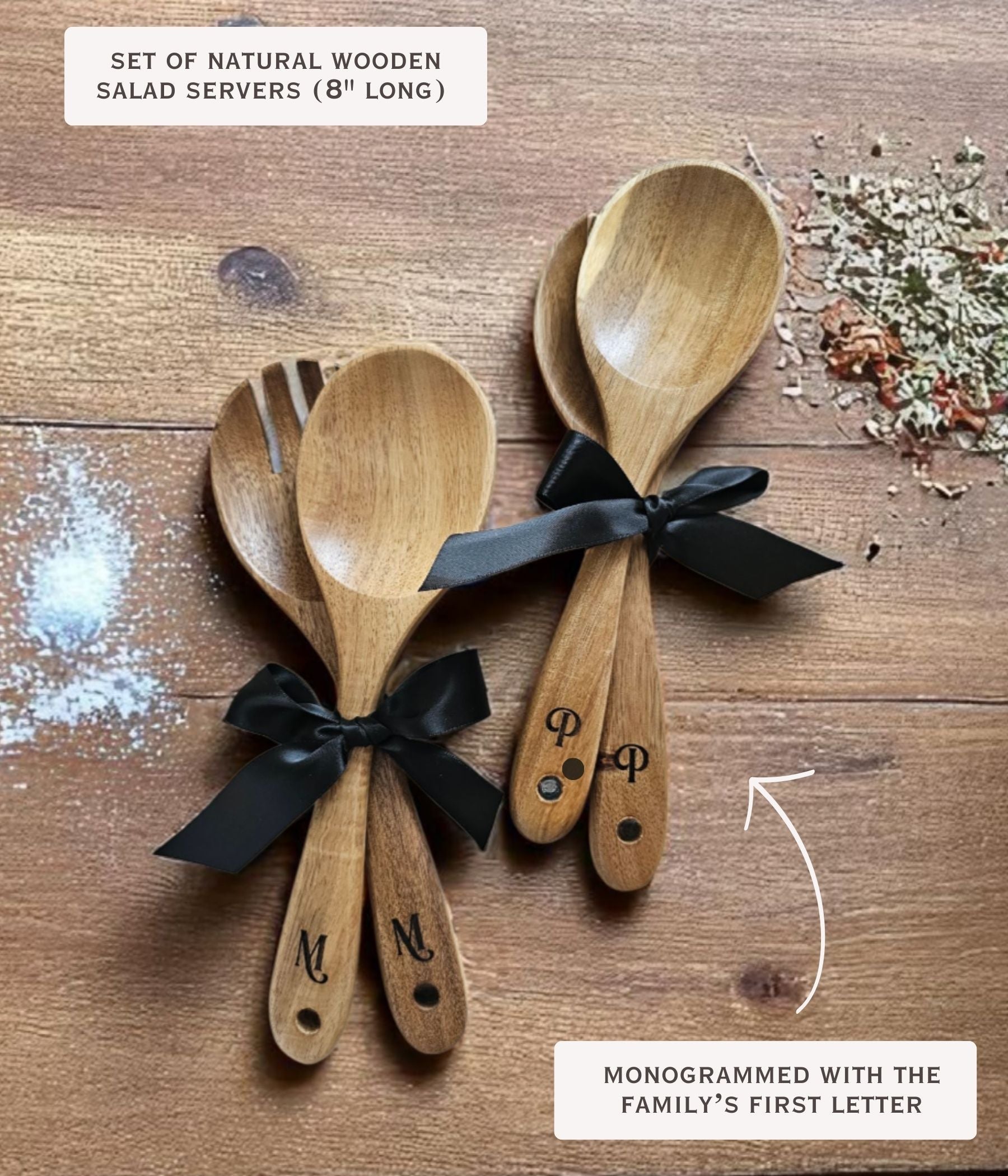 Set of natural wooden salad servers with black bows and monograms on a wooden surface.