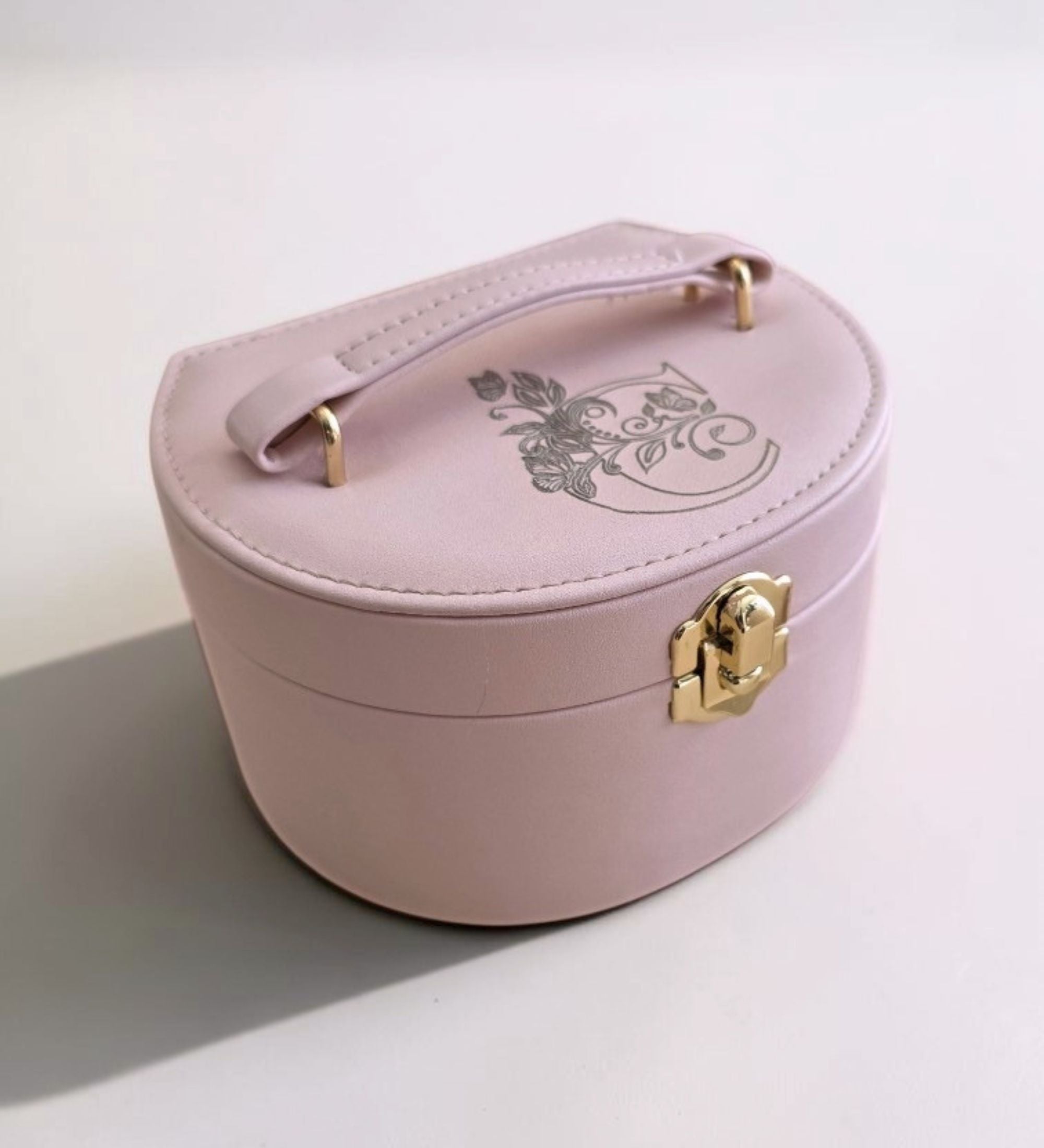 Pink leatherette personalized jewelry box closed, gold latch and carry handle visible, engraved butterfly-font initial "C" on lid