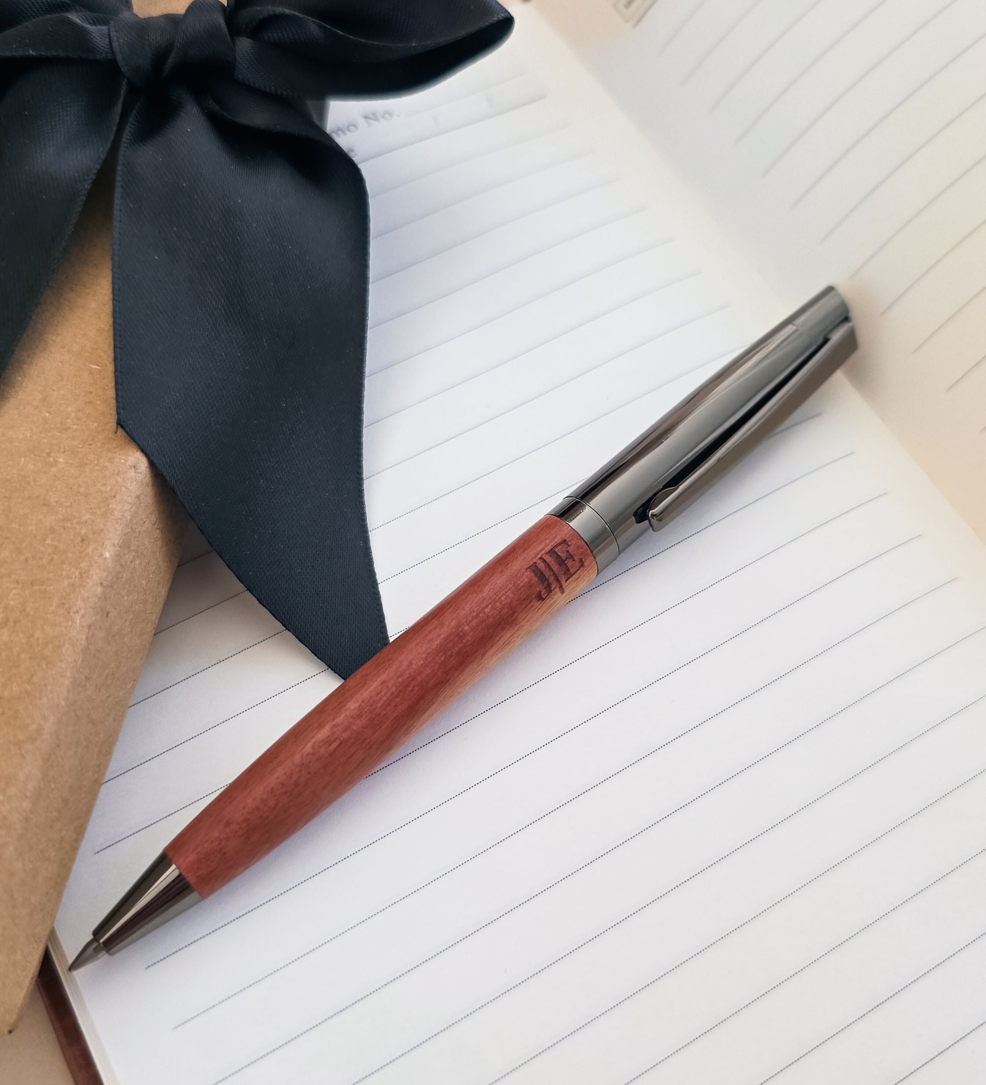 Personalized acacia wood pen laser-etched with initials, resting in a kraft gift box with black velvet insert and satin ribbon