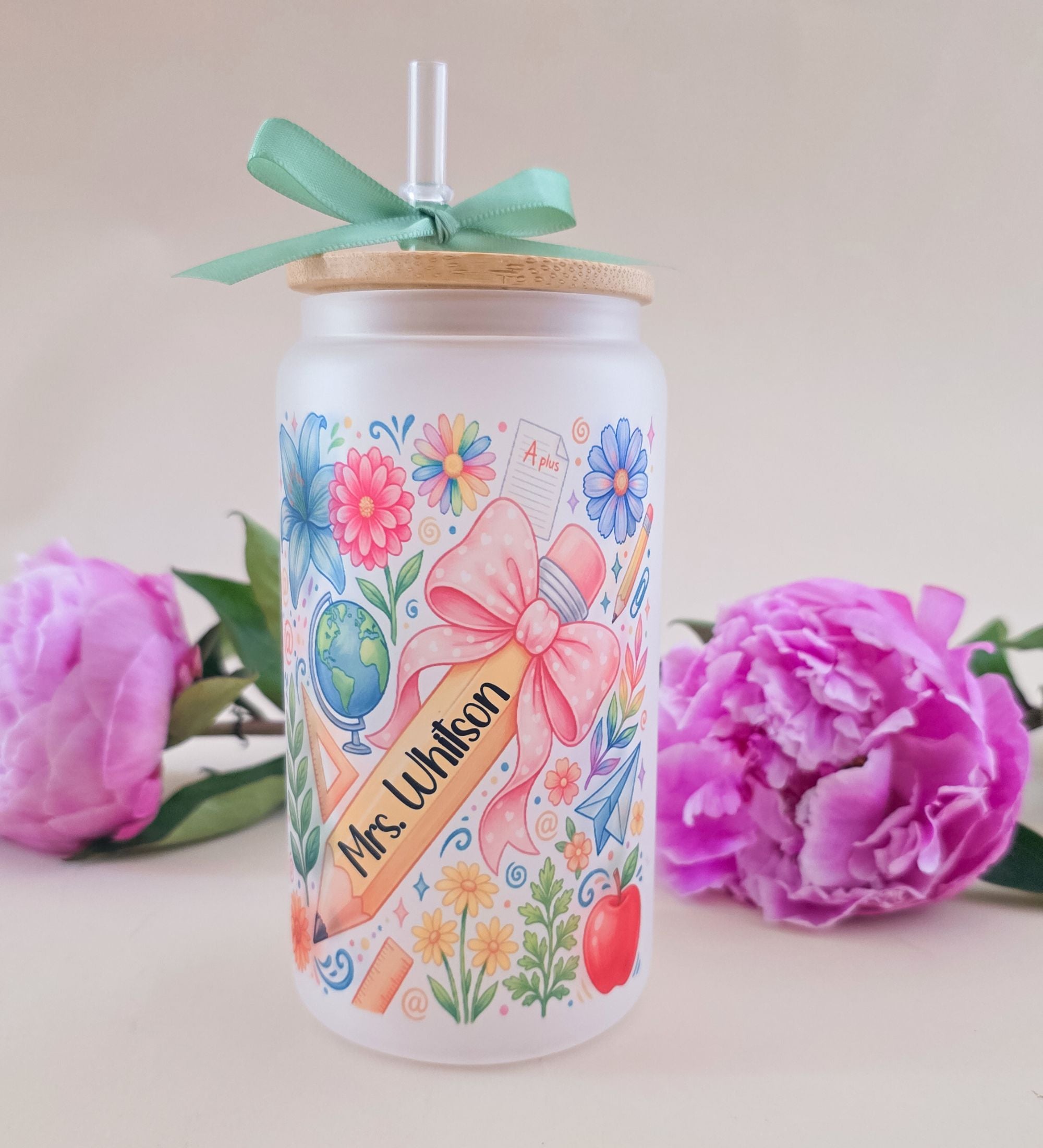 Personalized 16 oz frosted glass coquette floral teacher tumbler with Mrs. Whitson name banner, pink bow motif, pencil apple globe daisy design, bamboo lid with teal ribbon bow and acrylic straw, styled with pink peonies