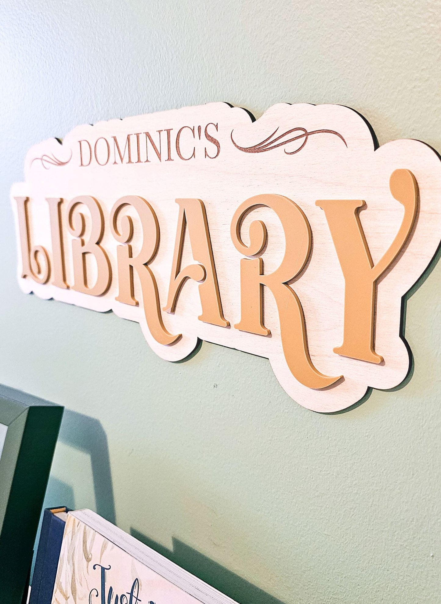 May include: A wooden sign with the words &#39;Dominic&#39;s Library&#39; in a brown font. The sign has a decorative swirl design on the top right corner.