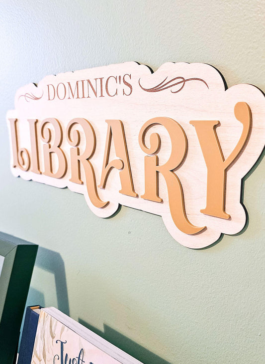 May include: A wooden sign with the words &#39;Dominic&#39;s Library&#39; in a brown font. The sign has a decorative swirl design on the top right corner.