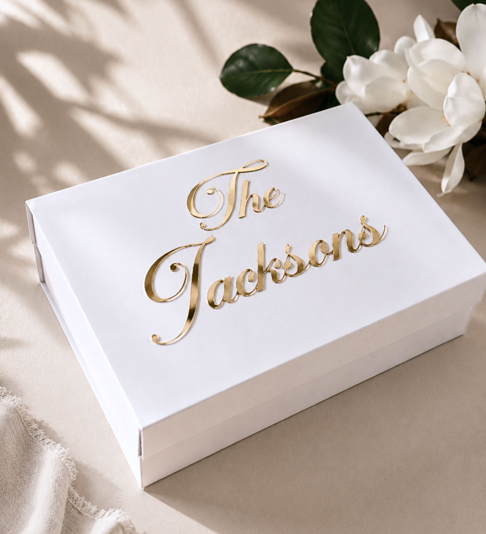 Personalized wedding memory box in white with the family name in raised gold acrylic script, held by a couple in formal attire
