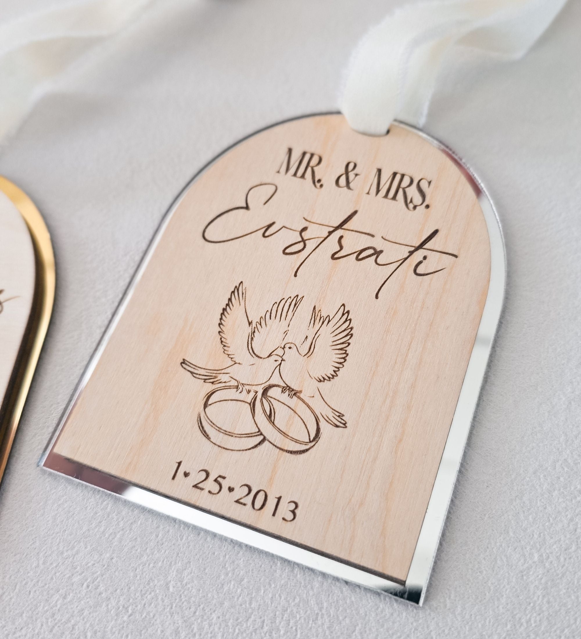 Close detail of the laser-etched dove and wedding ring motif beneath a script family name on natural birch