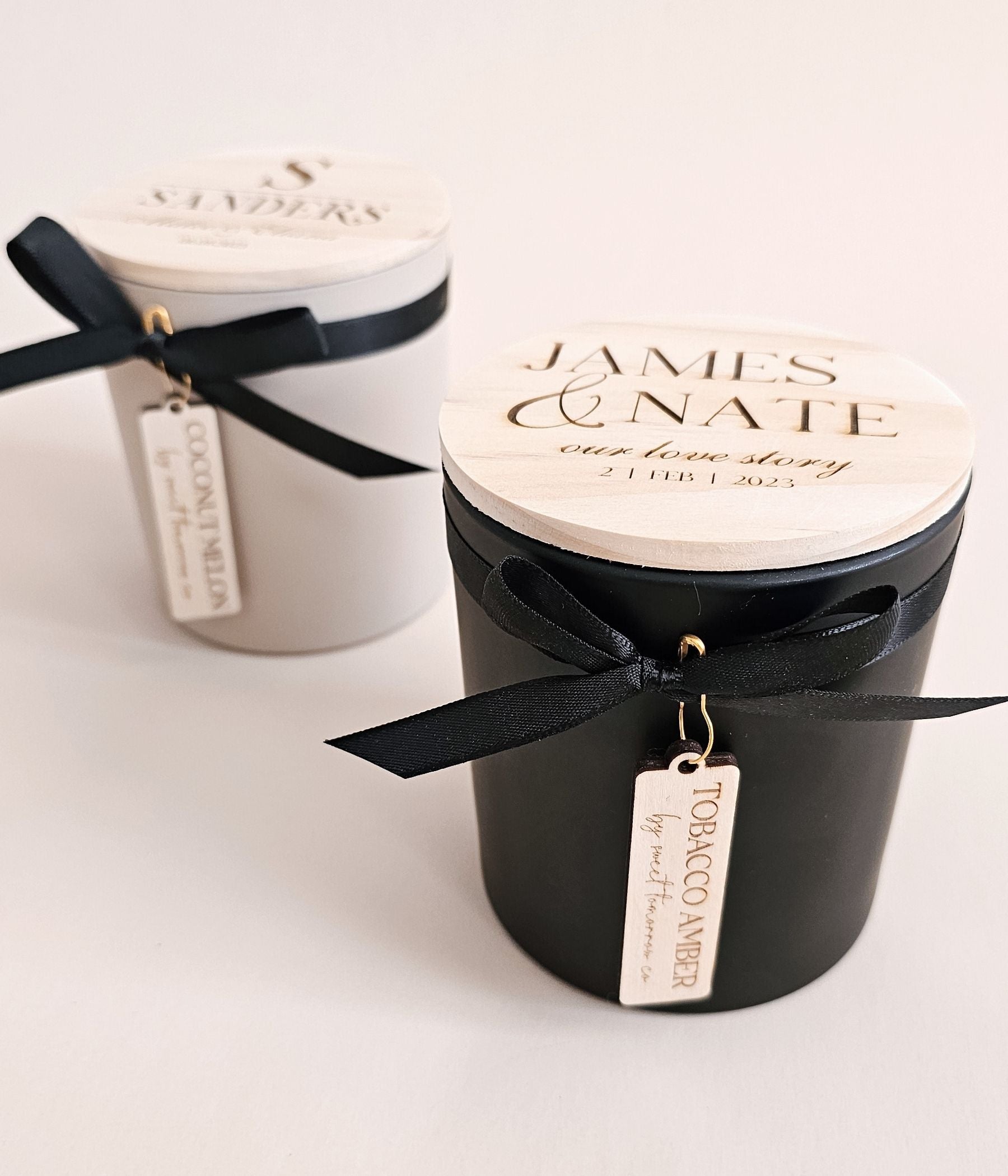 Two engraved lid candles showing different personalization designs for names and dates