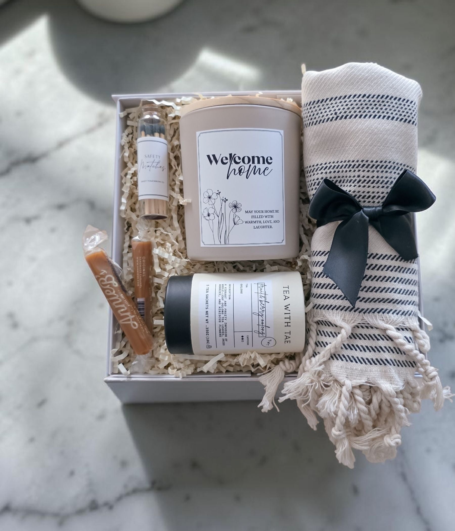 New home gift box showing Deluxe option with soy candle, Turkish towel, tea tin, safety matches, and caramel candies