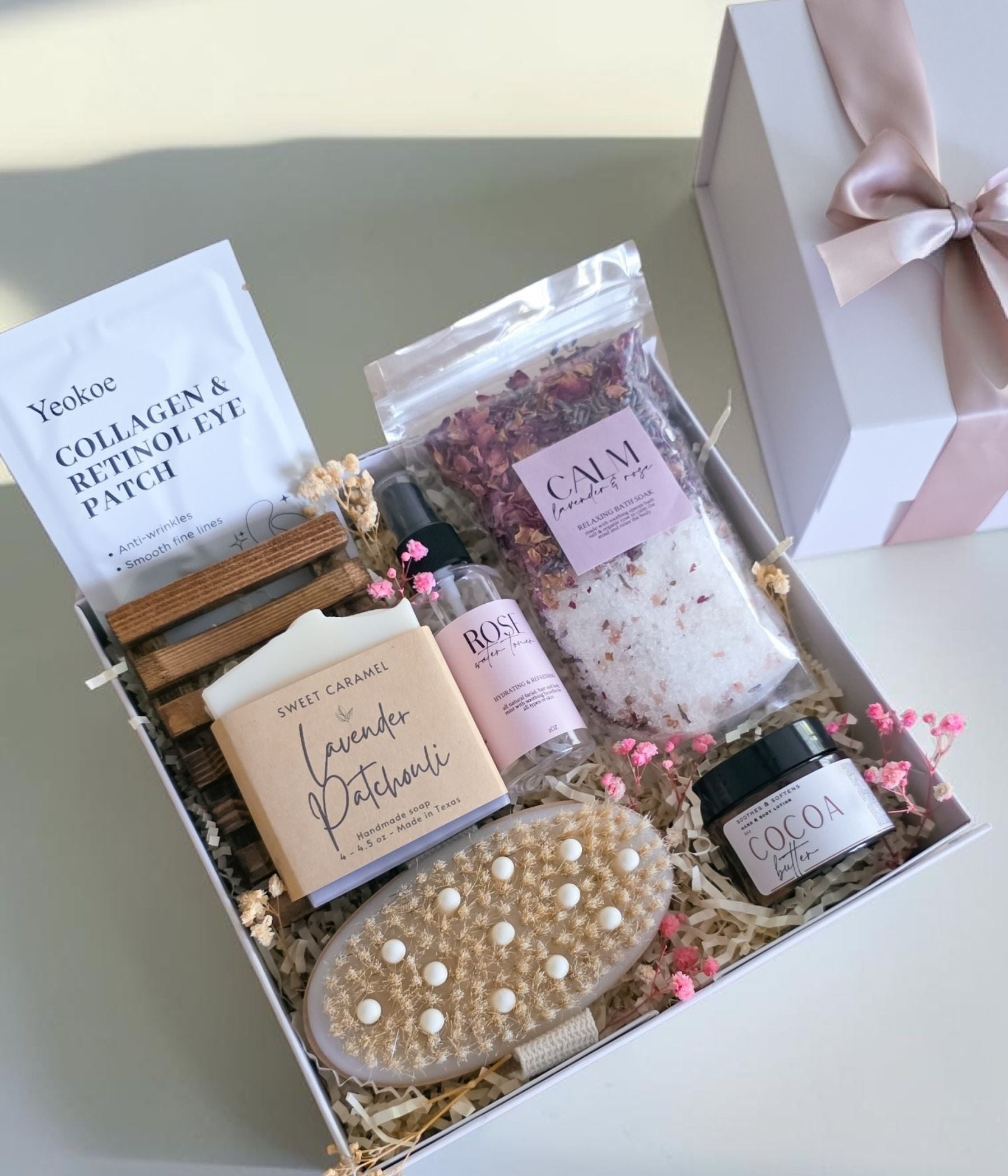 Luxury spa gift box for her open from above, showing bath soak, artisan soap on its wooden tray, facial mist, body cream, dry brush and eye patches arranged inside