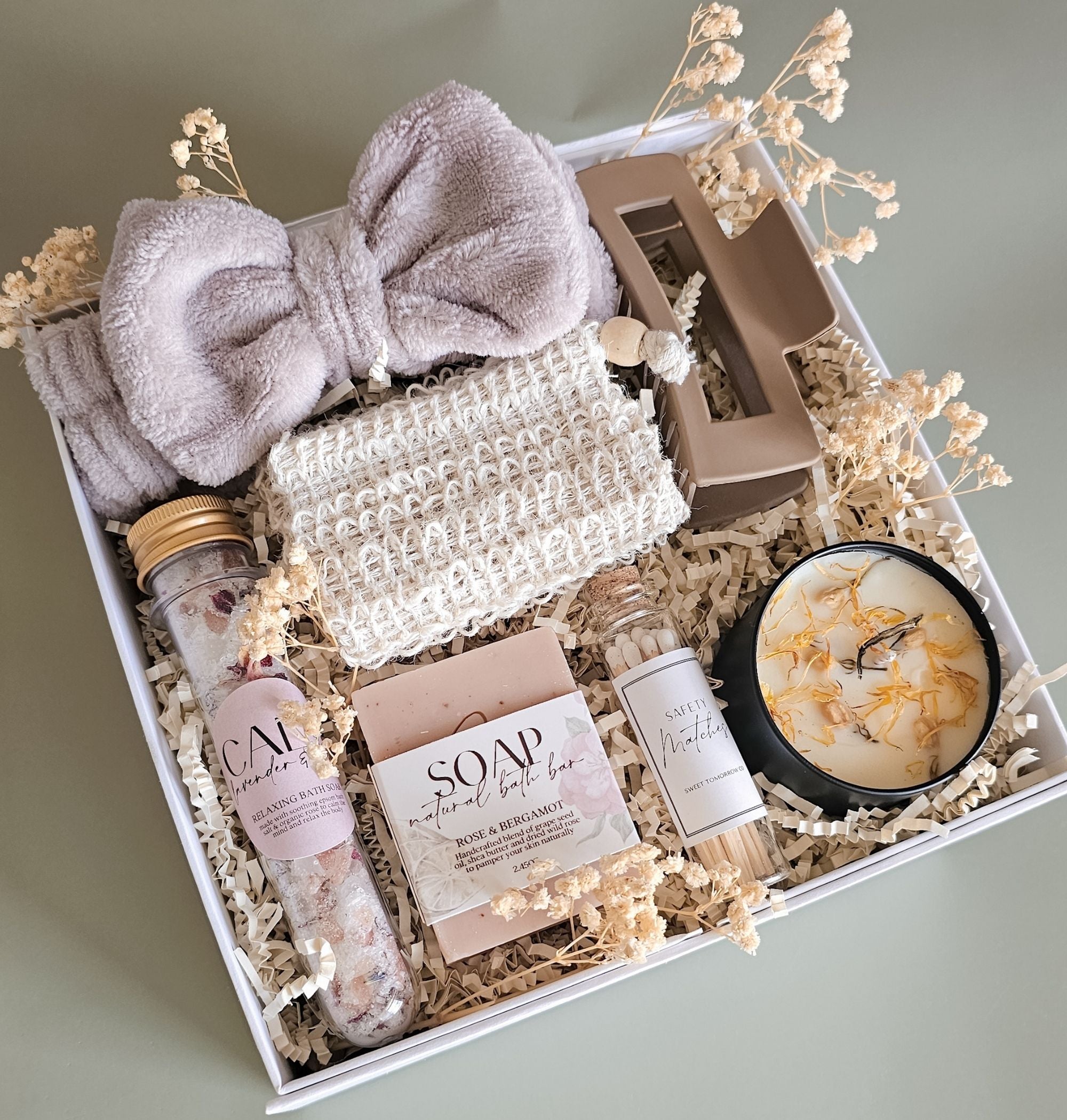 Open gift box showing full contents of The Botanical Box: soy wax candle with botanical topping, natural soap bar with sisal sleeve, lavender rose bath soak tube, spa headband, hair clip, glass jar matches in crinkle paper