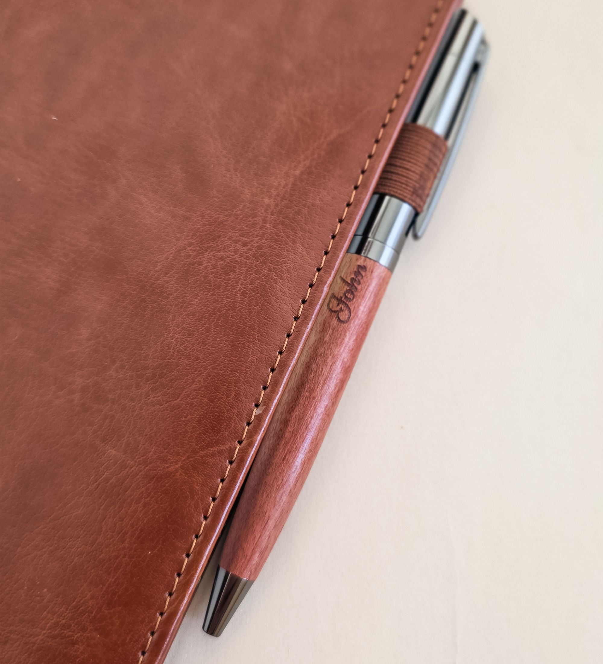 Acacia pen etched with a first name, held in the pen loop of a tan leather journal